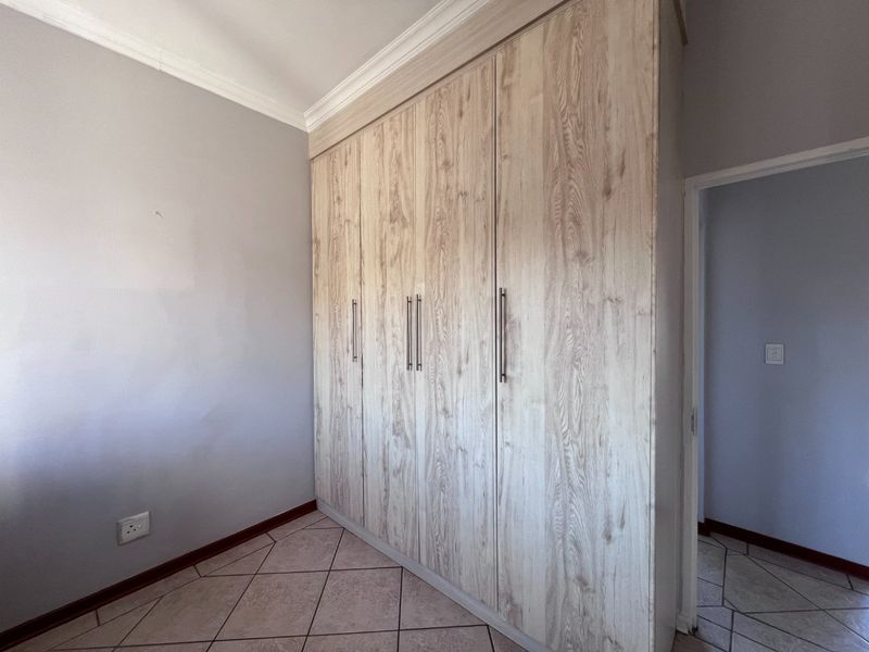 A clean, empty bedroom featuring light wood-grain built-in cupboards, neutral wall finishes, and tiled flooring.