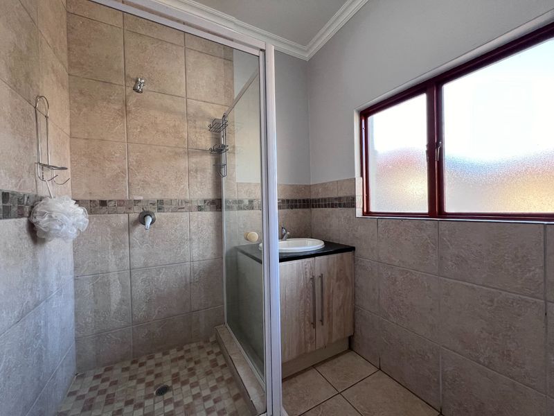 A functional bathroom featuring a tiled shower enclosure, a vanity cabinet with a basin, and an obscured glass window for privacy.