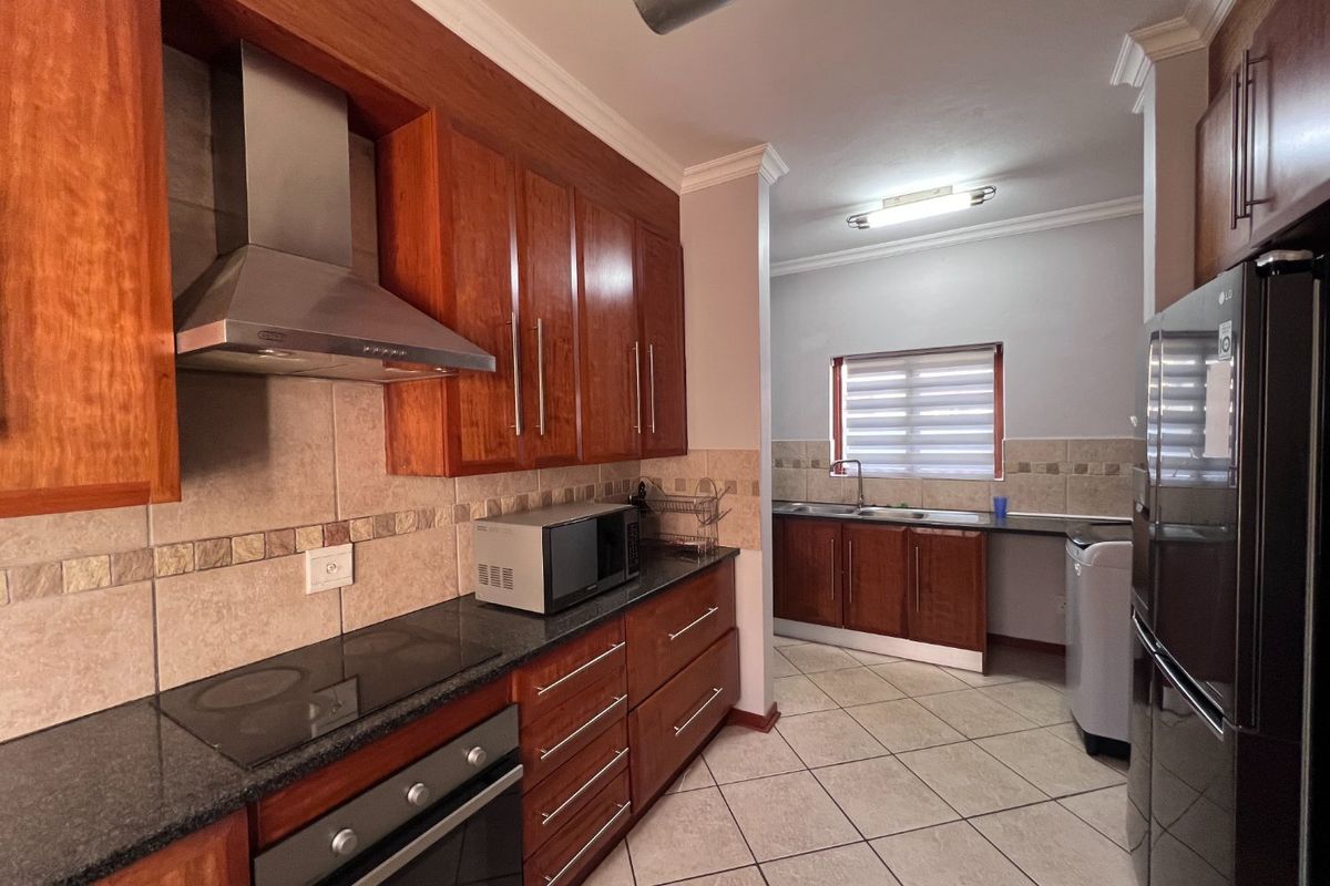 A functional kitchen featuring warm-toned wooden cabinetry, granite countertops, integrated appliances, and a separate scullery area with a double sink.