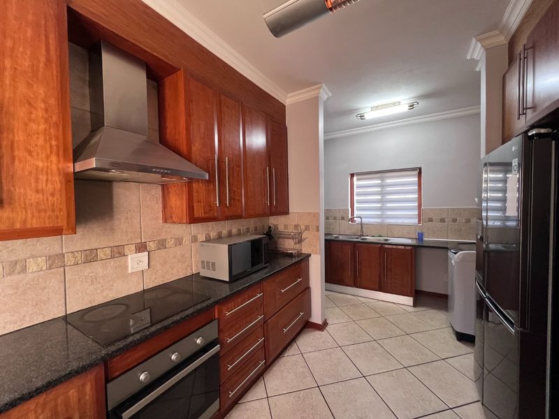 A functional kitchen featuring warm-toned wooden cabinetry, granite countertops, integrated appliances, and a separate scullery area with a double sink.