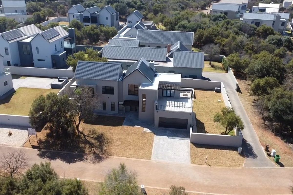Aerial view of a modern double-story residential property featuring a metal roof, solar panels, paved driveway, and enclosed garden area.
