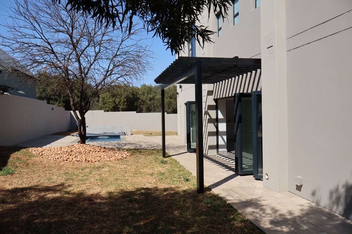 Rear exterior view featuring a paved patio with a modern pergola, bi-fold doors leading inside, and a swimming pool in the garden.
