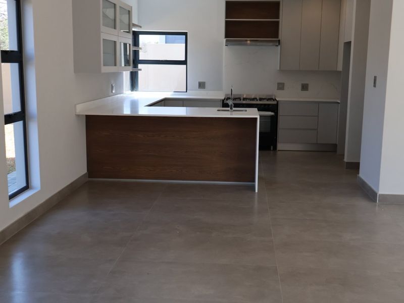 Modern, open-plan kitchen featuring sleek cabinetry, stone countertops, a functional island, and high-quality tiled flooring in a clean, contemporary space.