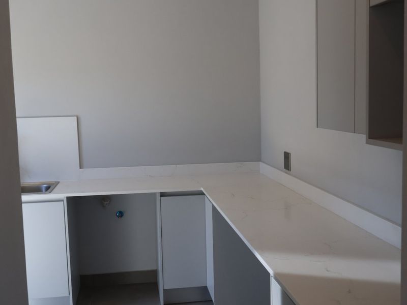 A modern, clean scullery featuring stone countertops, built-in cabinetry, and tiled flooring, providing a functional and organized secondary kitchen or utility space.