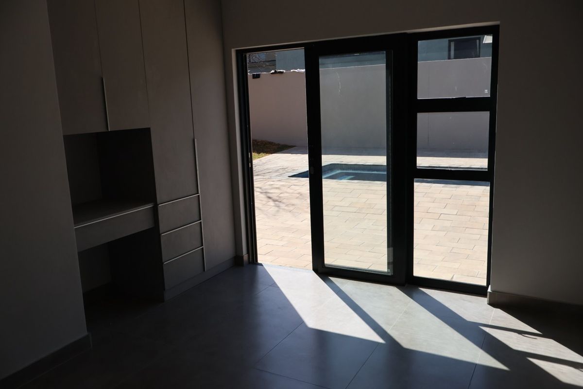 A modern, empty bedroom featuring built-in cabinetry, large format floor tiles, and a sliding glass door providing direct access to the patio and pool area.