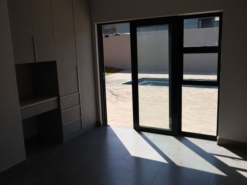 A modern, empty bedroom featuring built-in cabinetry, large format floor tiles, and a sliding glass door providing direct access to the patio and pool area.