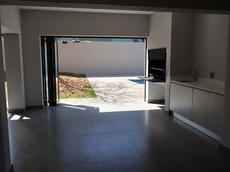 Modern open-plan entertainment area featuring a built-in braai, kitchenette cabinetry, and seamless access to the outdoor patio and pool area through bi-fold doors.