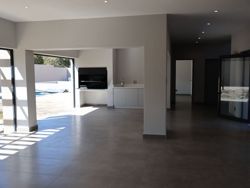 Spacious open-plan living area featuring a built-in braai, kitchenette, and seamless access to the outdoor pool area through large sliding glass doors.