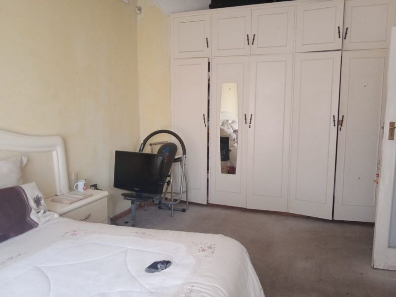 A bedroom featuring built-in cupboards with integrated mirror and carpeted flooring, offering a functional space with potential for cosmetic updates.