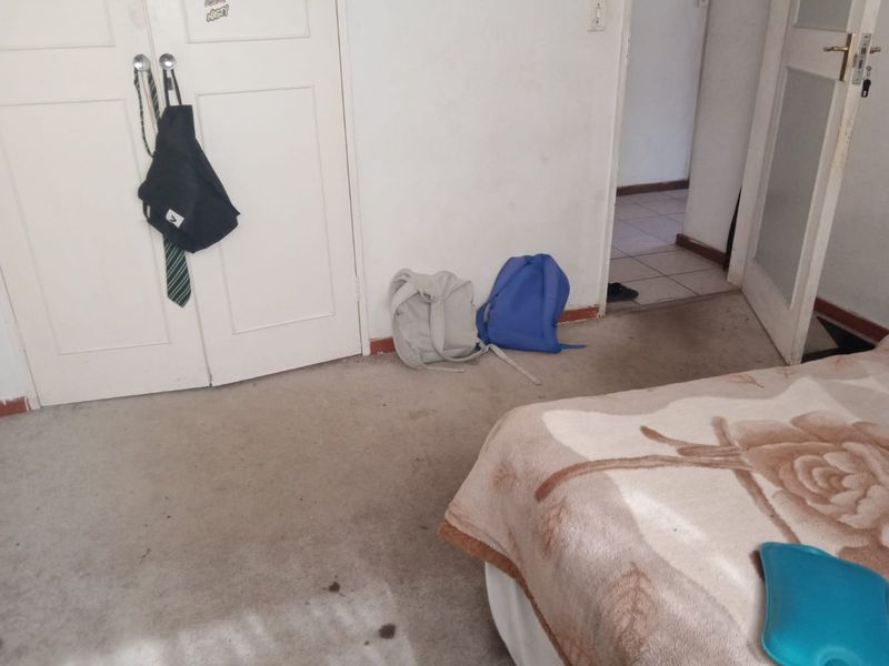 A bedroom featuring built-in cupboards and carpeted flooring, showing signs of wear and tear.