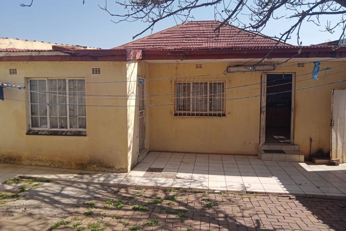 Rear view of the property featuring a tiled patio area, security bars on windows, and a tiled roof structure requiring maintenance.