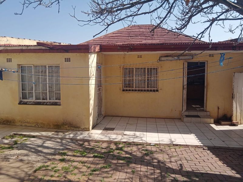 Rear view of the property featuring a tiled patio area, security bars on windows, and a tiled roof structure requiring maintenance.