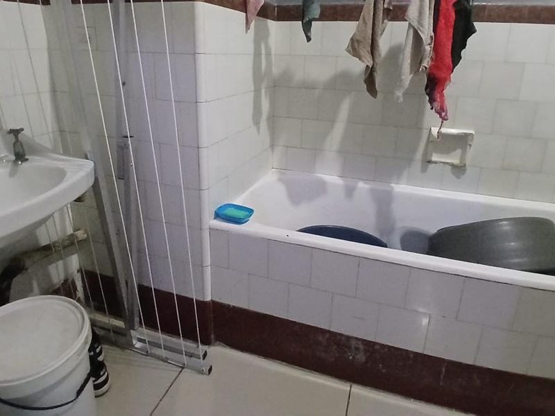 A dated bathroom featuring a pedestal basin and a tiled bathtub, requiring cosmetic updates and maintenance to improve its overall condition and appeal.