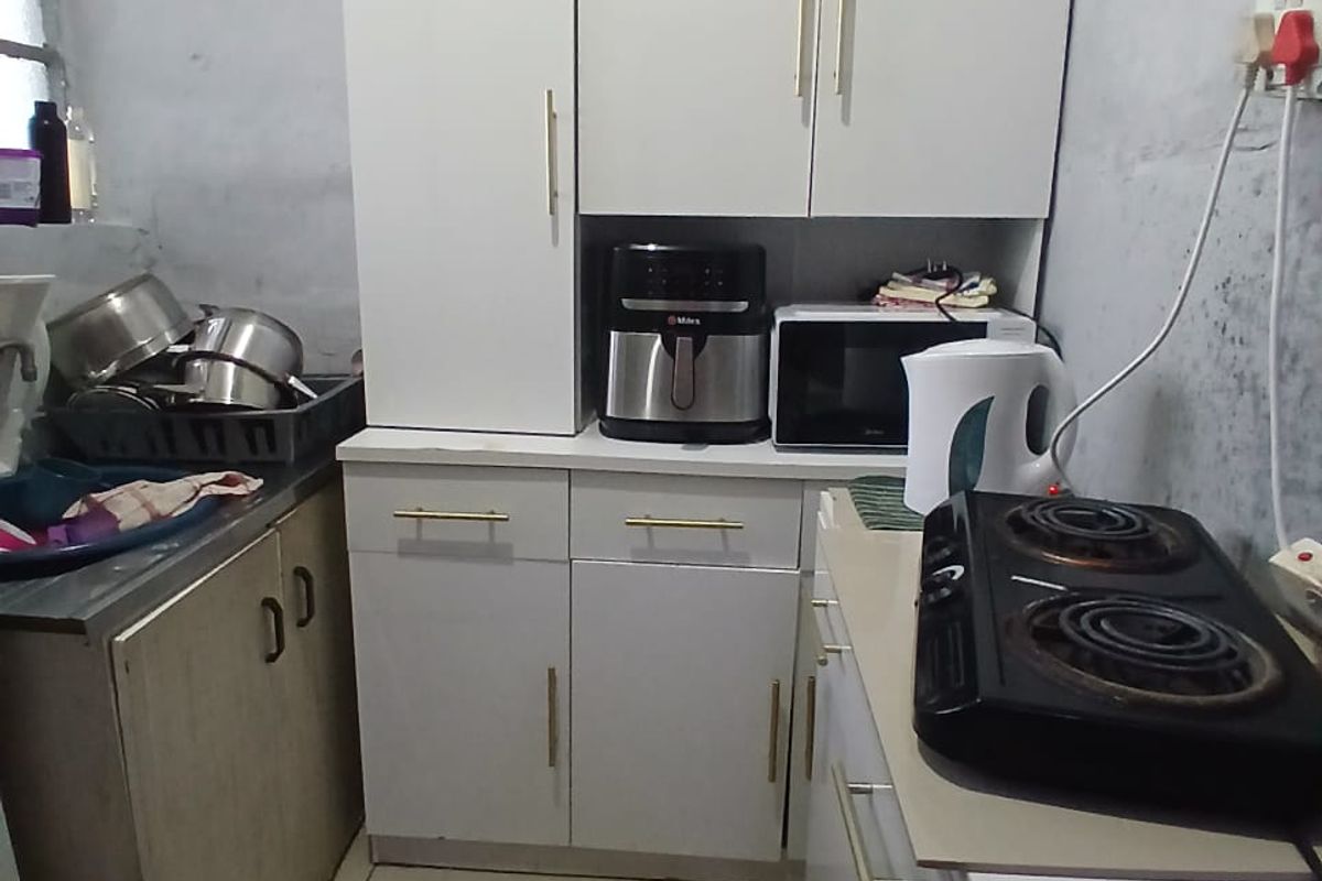 A compact kitchen area featuring white cabinetry, tiled flooring, and a sink, currently requiring wall finishing and maintenance to improve the overall aesthetic.