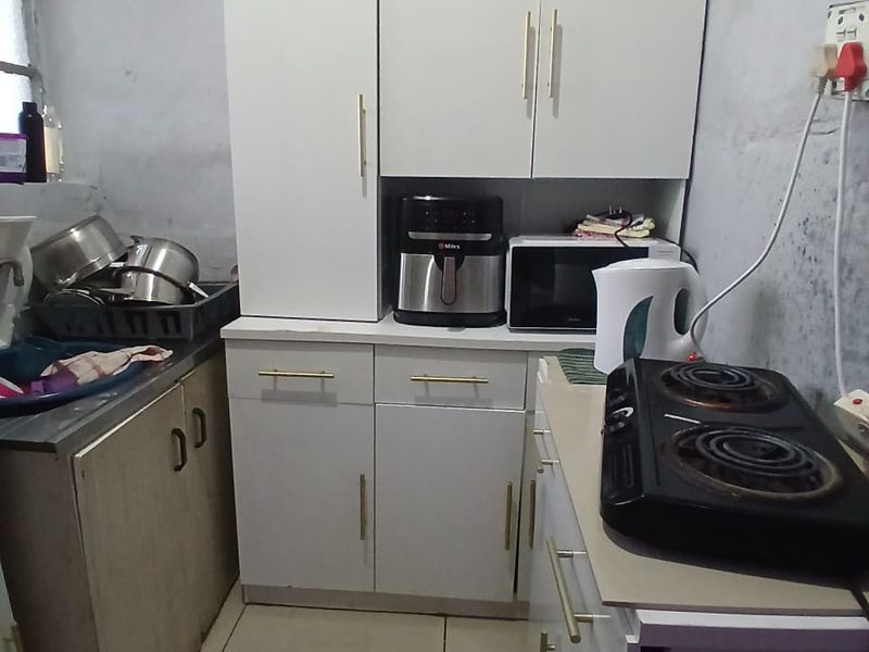 A compact kitchen area featuring white cabinetry, tiled flooring, and a sink, currently requiring wall finishing and maintenance to improve the overall aesthetic.