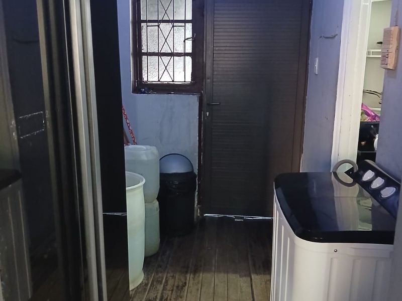 A functional laundry area featuring timber flooring, a security door, and a window with burglar bars, requiring cosmetic updates to improve its condition.