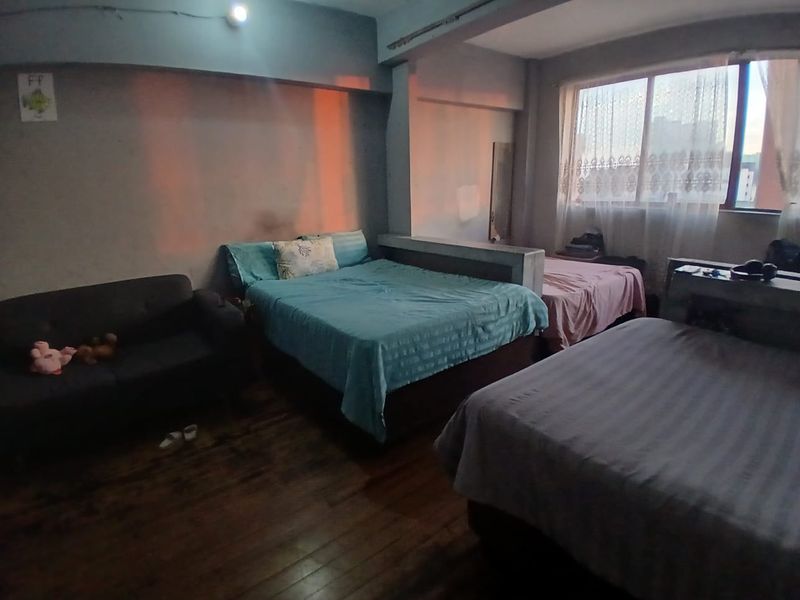 A spacious bedroom featuring hardwood flooring, a large window for natural light, and a built-in partition wall separating sleeping areas.