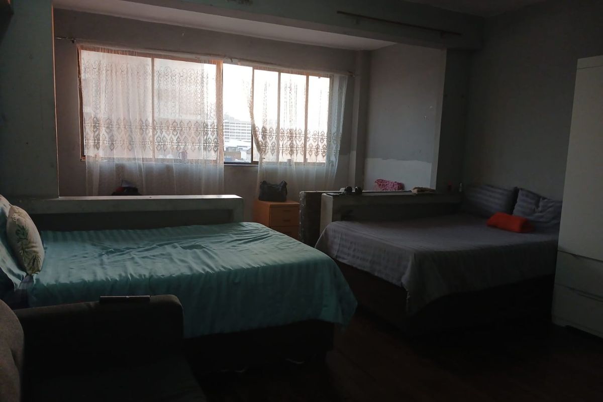 A spacious bedroom featuring a large window with natural light, requiring cosmetic updates to the wall finishes to improve the overall aesthetic.