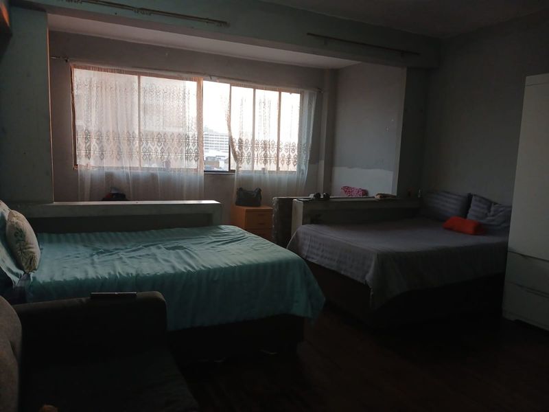 A spacious bedroom featuring a large window with natural light, requiring cosmetic updates to the wall finishes to improve the overall aesthetic.