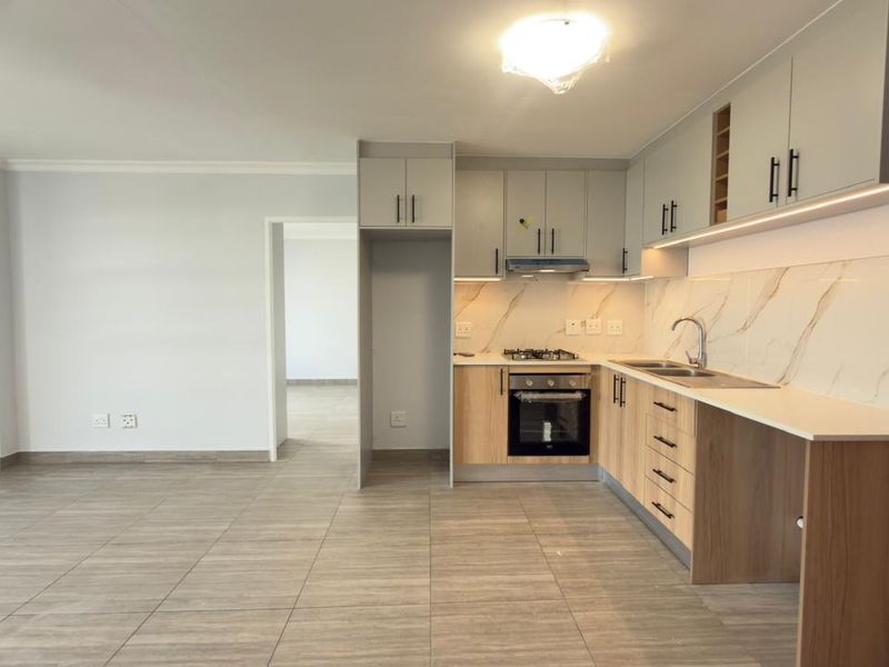 Modern open-plan kitchen featuring contemporary cabinetry, integrated appliances, marble-look splashback, and sleek tiled flooring in a bright, spacious living area.