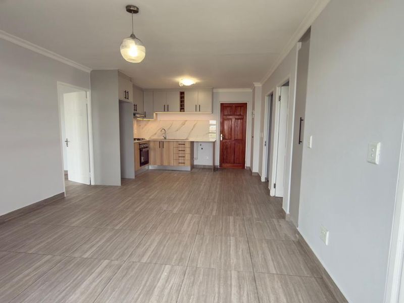 Spacious open-plan living area featuring a modern kitchen with built-in cabinetry, stone countertops, and tiled flooring throughout.