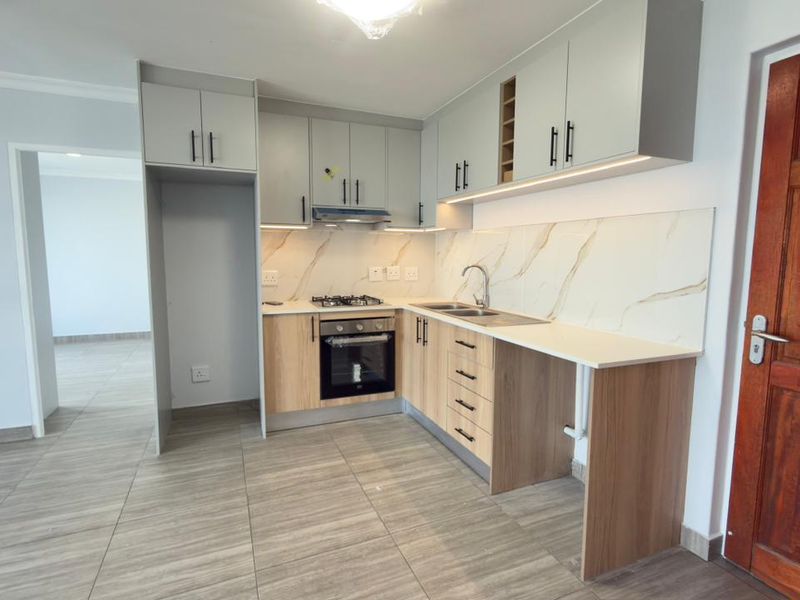 Modern kitchen featuring light wood and grey cabinetry, marble-look splashback, gas hob, electric oven, and tiled flooring in an open-plan layout.