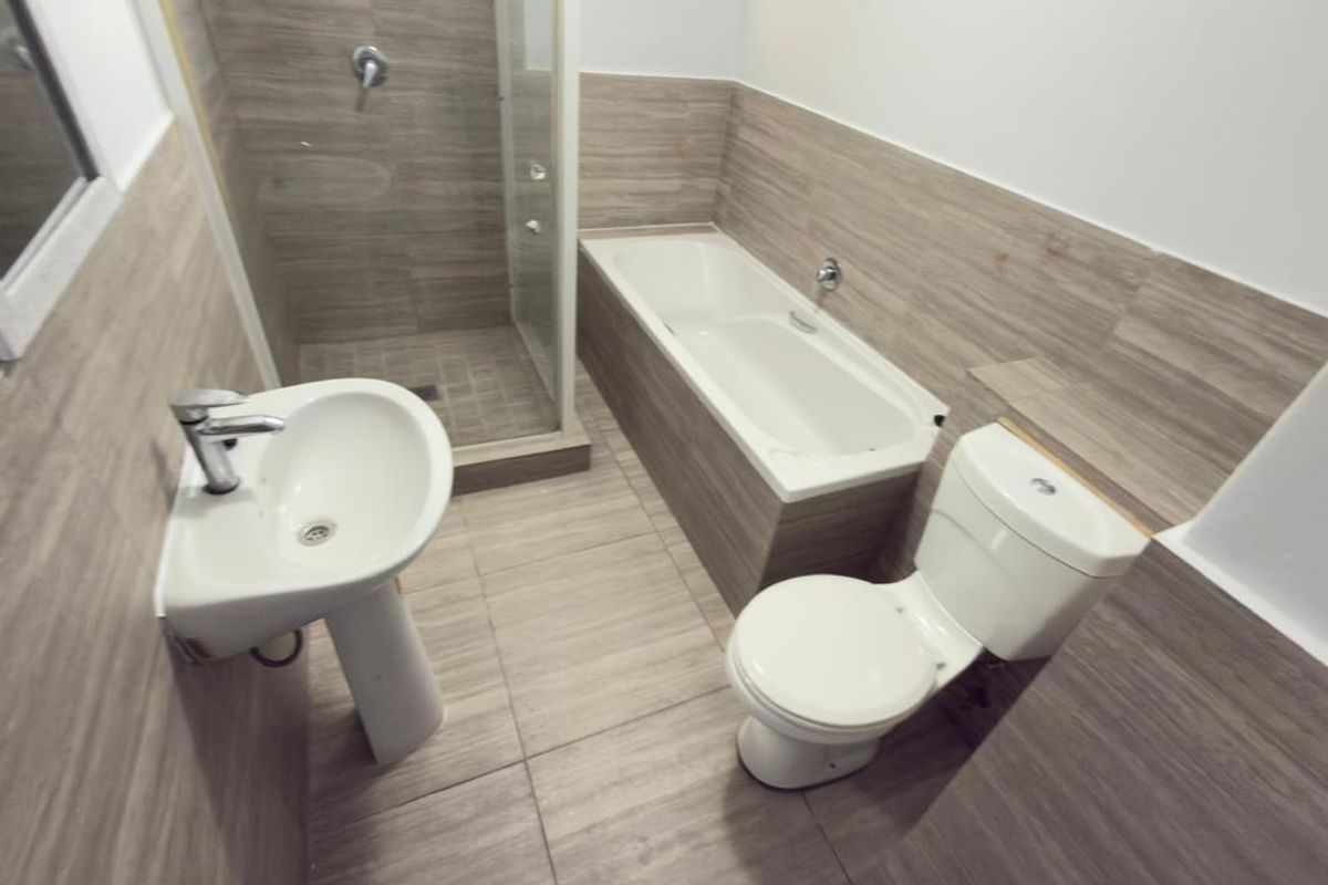 Modern bathroom featuring a pedestal washbasin, a separate shower enclosure, a bathtub, and a toilet, finished with neutral wood-look wall and floor tiles.