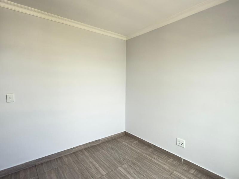 A clean, empty bedroom featuring modern wood-look tiled flooring, neutral walls, and a built-in cupboard with a contemporary finish.
