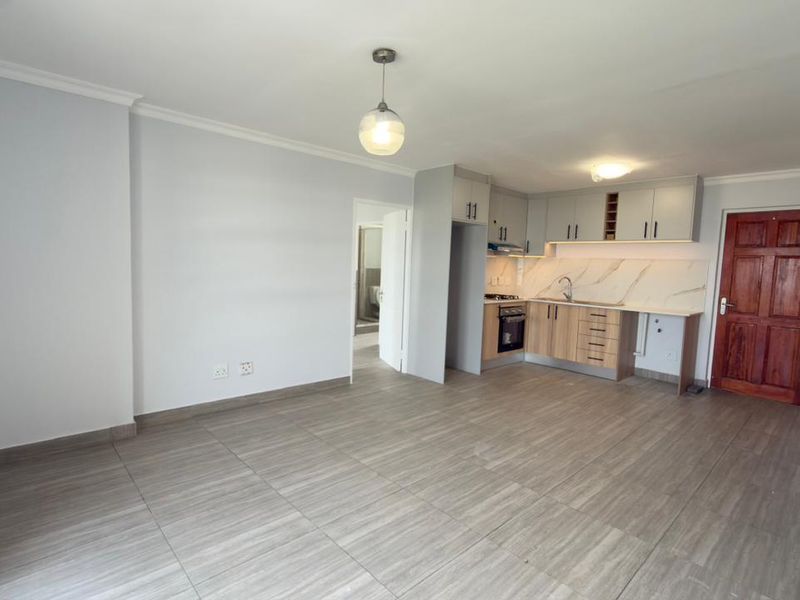 An open-plan living and kitchen area featuring modern cabinetry, integrated appliances, tiled flooring, and neutral finishes, providing a clean and versatile living space.