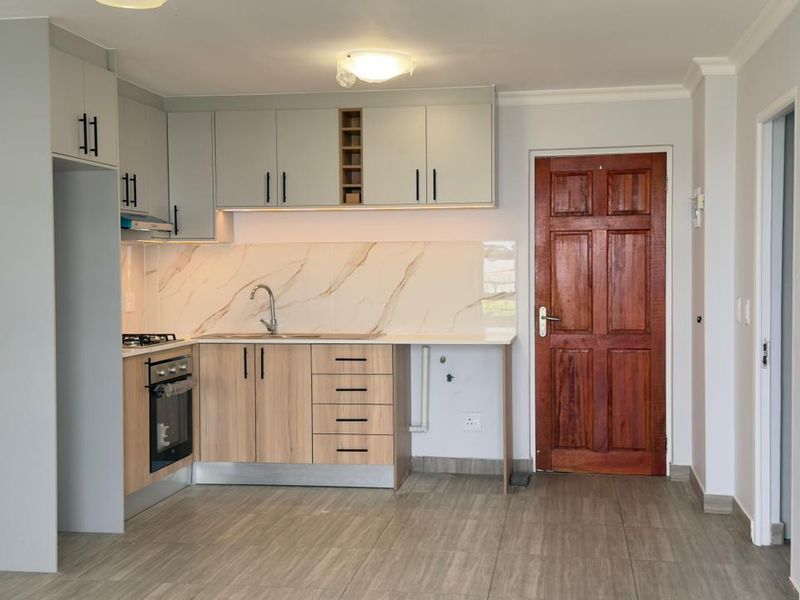 Modern kitchen featuring light wood and grey cabinetry, marble-look backsplash, built-in oven, gas hob, and tiled flooring in an open-plan layout.