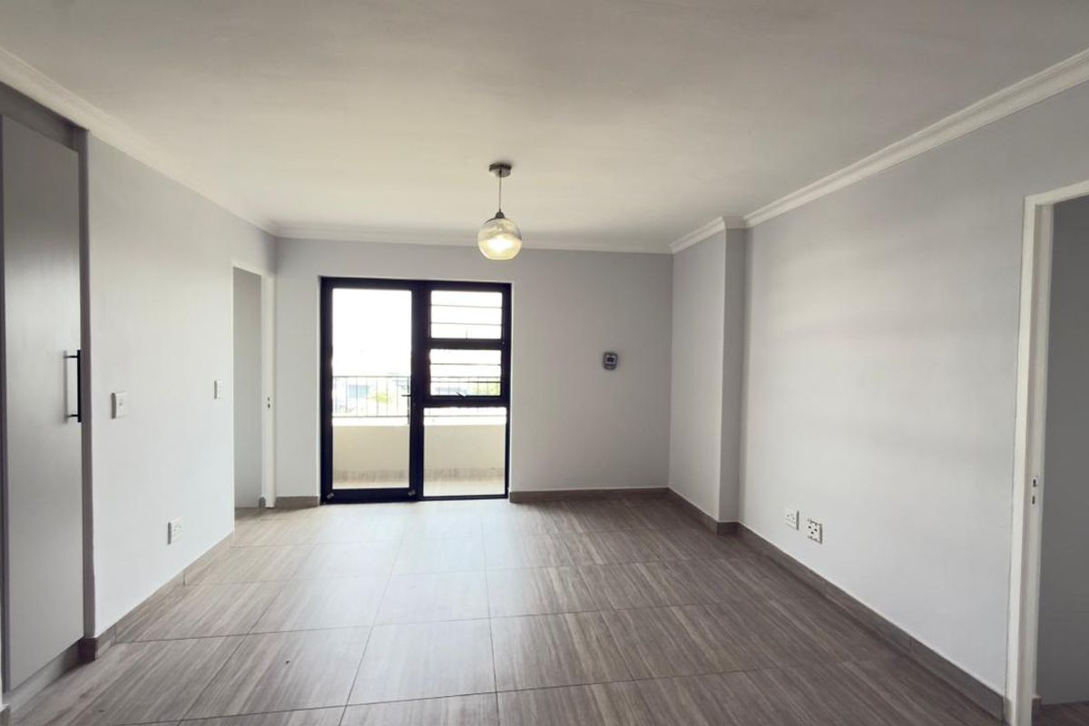 A bright, empty living area featuring modern tiled flooring, neutral walls, and a sliding glass door providing access to an outdoor balcony.