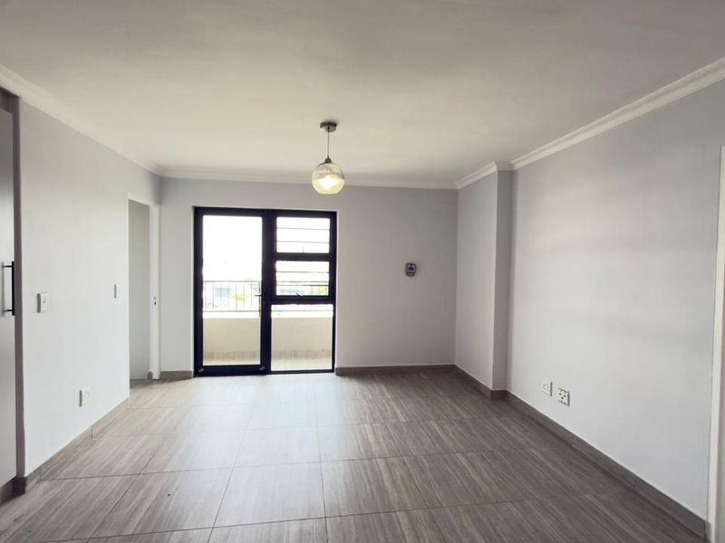 A bright, empty living area featuring modern tiled flooring, neutral walls, and a sliding glass door providing access to an outdoor balcony.