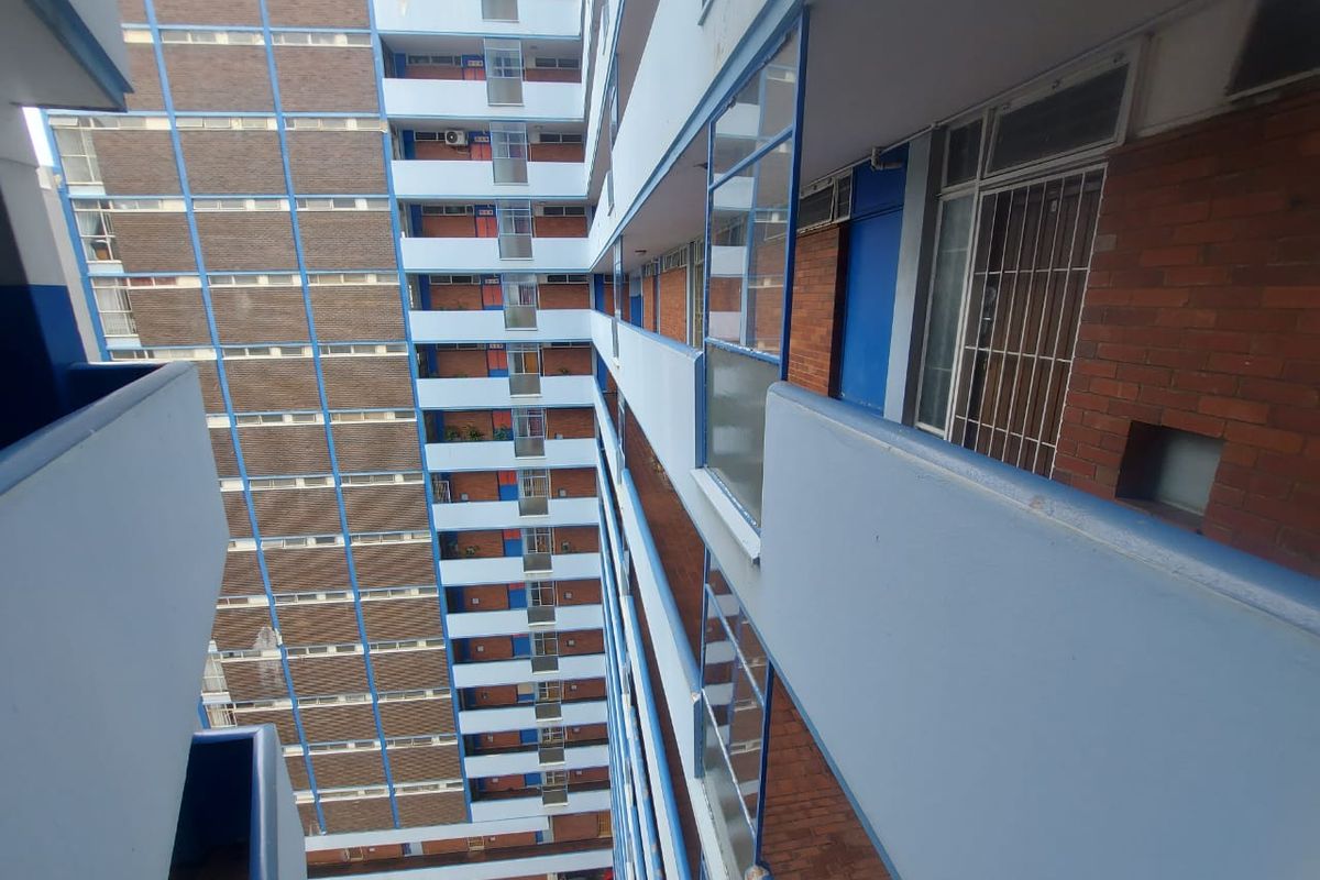 View of the apartment building exterior, showcasing the brick facade, external walkways, and balcony structures of the multi-story residential complex.