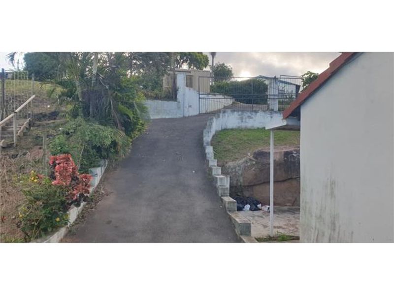A view of the property driveway featuring a paved surface, retaining walls, and a gated entrance leading to the residence.