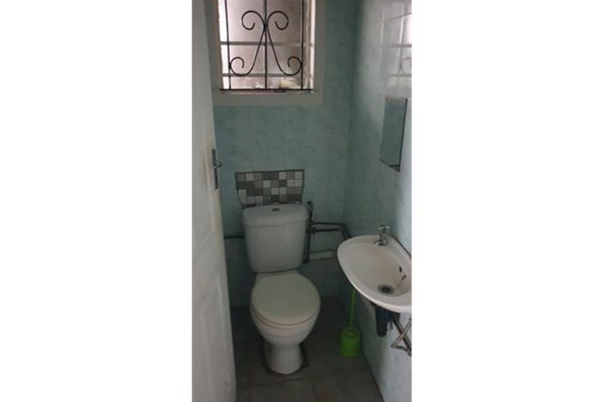 A compact guest bathroom featuring a toilet, wall-mounted basin, and tiled finishes, requiring cosmetic updates to improve its dated appearance.