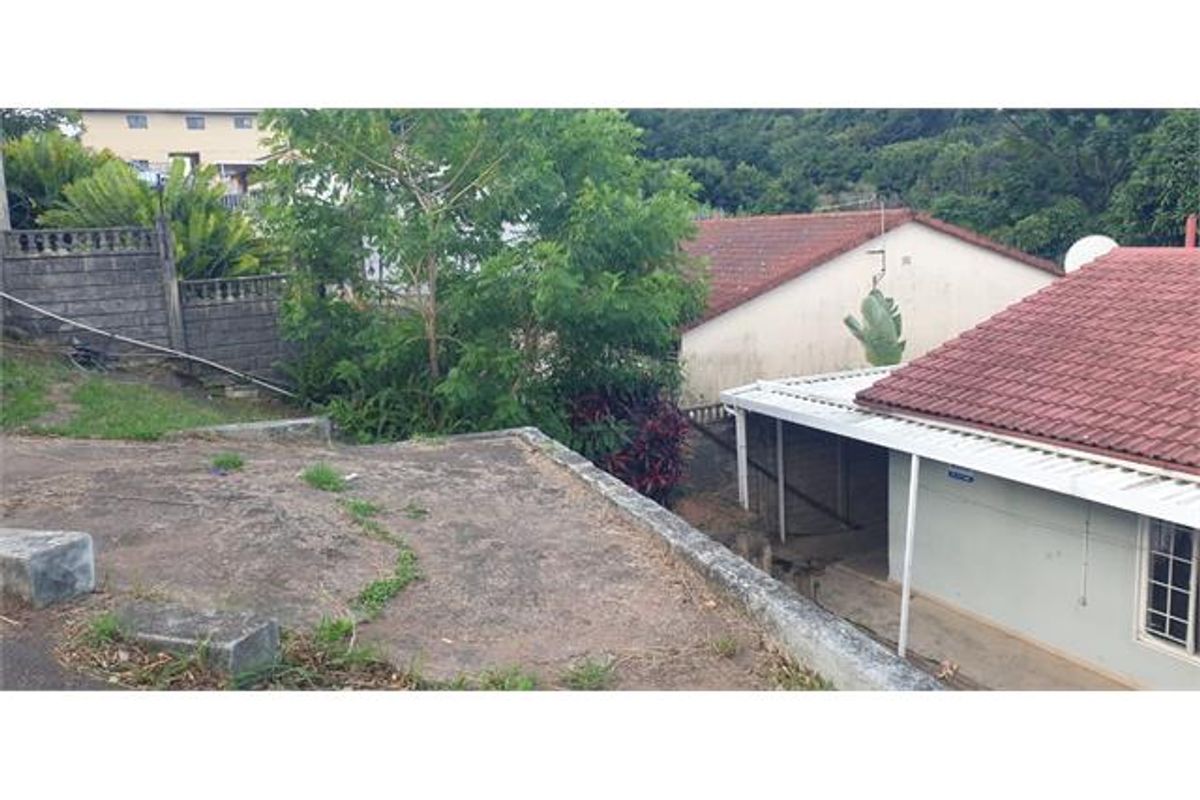 Rear exterior view showing a concrete retaining wall, tiled roof structure, and a covered patio area with surrounding garden space.