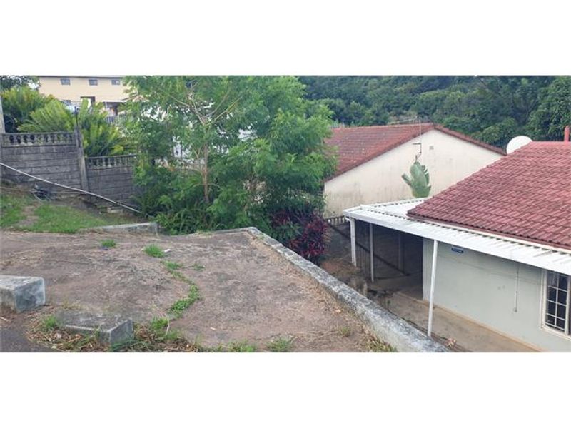 Rear exterior view showing a concrete retaining wall, tiled roof structure, and a covered patio area with surrounding garden space.