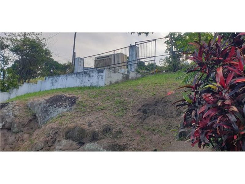 An exterior view of a sloped property featuring a stone embankment, concrete retaining wall, and metal perimeter fencing.