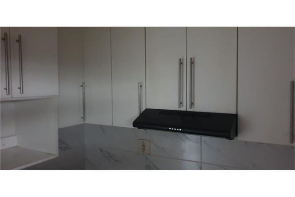 A close-up view of modern white kitchen cabinetry featuring a black extractor fan and marble-look tiled backsplash.