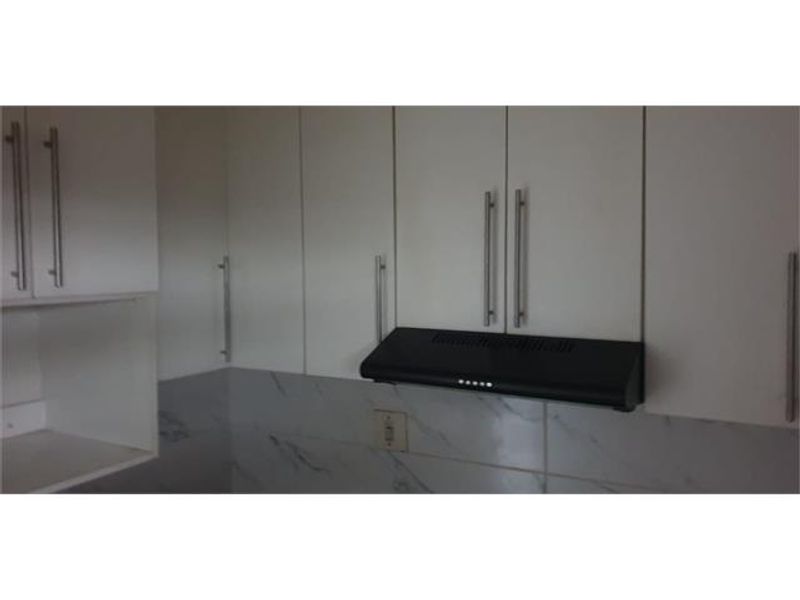 A close-up view of modern white kitchen cabinetry featuring a black extractor fan and marble-look tiled backsplash.