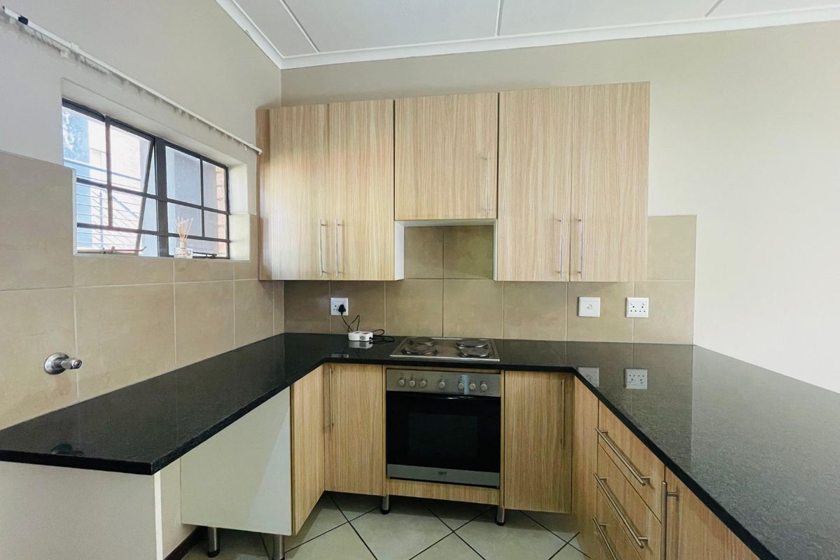 A clean, functional kitchen featuring light wood-finish cabinetry, dark granite countertops, a built-in oven and hob, and neutral tiled backsplash.