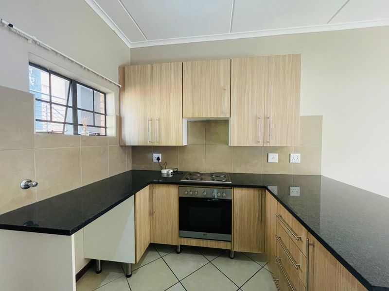A clean, functional kitchen featuring light wood-finish cabinetry, dark granite countertops, a built-in oven and hob, and neutral tiled backsplash.