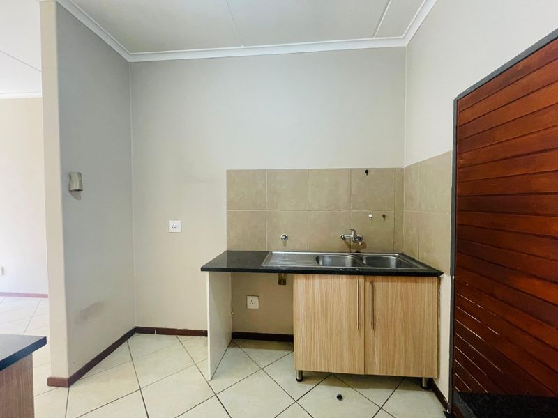 A compact kitchen area featuring a double bowl sink, granite countertop, tiled splashback, and light wood-finish base cabinetry.