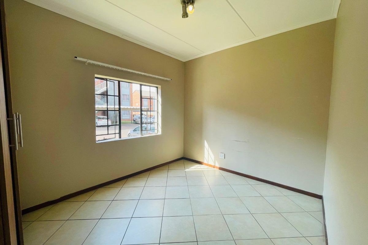 An empty bedroom featuring tiled flooring, a built-in cupboard, and a window fitted with security bars.
