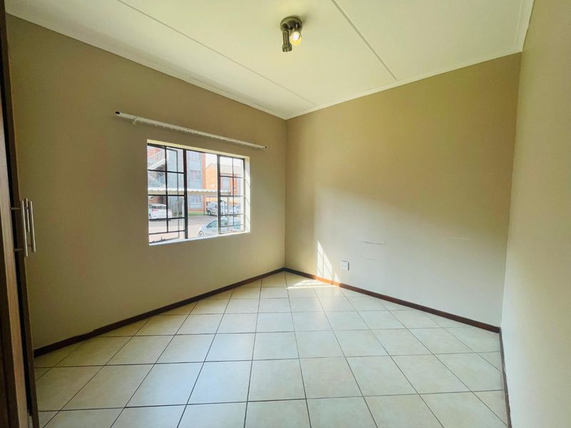 An empty bedroom featuring tiled flooring, a built-in cupboard, and a window fitted with security bars.