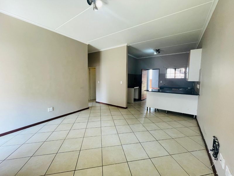 An open-plan living and kitchen area featuring neutral wall tones, tiled flooring, and a functional kitchen layout with a breakfast bar.