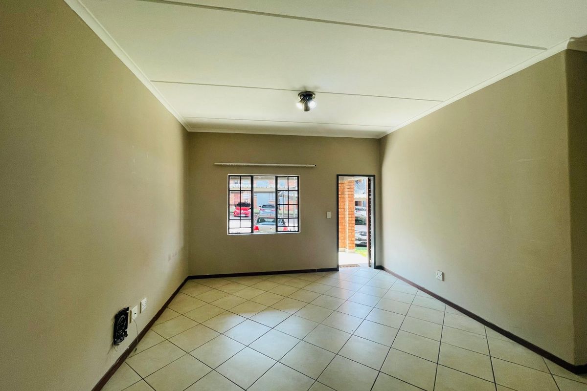 An empty, neutrally painted living room featuring tiled flooring, a window with security bars, and direct access to the exterior.
