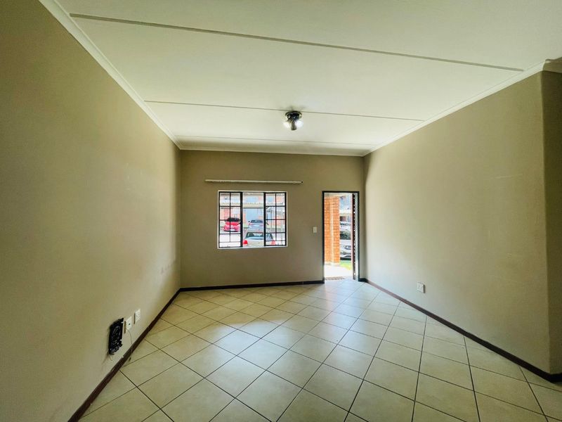 An empty, neutrally painted living room featuring tiled flooring, a window with security bars, and direct access to the exterior.