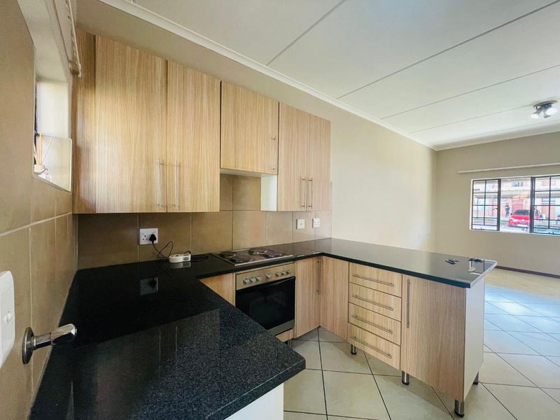 A clean, functional kitchen featuring light wood-finish cabinetry, black granite countertops, and built-in oven and hob, with neutral tiled flooring throughout.