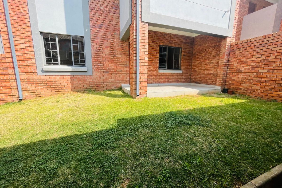 A private rear garden area featuring a small tiled patio, brick exterior walls, and security-fitted windows.